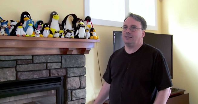 Linus Torvalds, créateur du noyau Linux, travaillant sur son bureau devant un ordinateur portable, avec plusieurs figures de pingouins de smoking à l'arrière-plan.